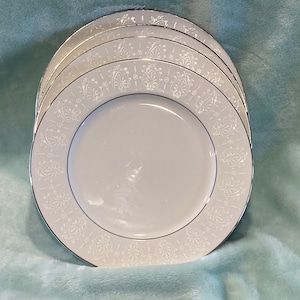 May include: A set of four white ceramic dinner plates with a silver rim and a delicate floral pattern.