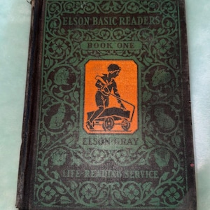 May include: Vintage "Elson Basic Readers Book One" book. The cover is dark green with ornate floral designs and the title in white. An orange rectangle features a boy pushing a cart. The book is from the "Life-Reading Service".