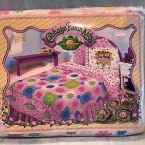 May include: Sealed Cabbage Patch Kids bedding set featuring a bed illustration with a purple bed frame, floral quilt, and pillow. The packaging has a floral border and the words "Cabbage Patch Kids".