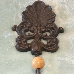 May include: A decorative cast iron hook with a scroll design and a wooden knob. The hook is painted in a dark brown color.