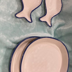 Puede incluir: Tres platos de cerámica con forma de pez con ribete azul. Los dos platos más pequeños están sobre una superficie azul claro y el plato más grande está encima de los más pequeños.