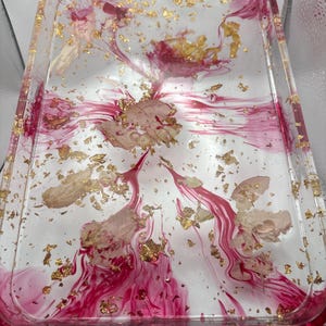 May include: A rectangular clear resin tray with a red and gold design. The tray features streaks of red and gold leaf accents, creating a decorative and artistic look. The tray is ideal for serving or displaying items.