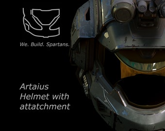 Può includere: Primo piano di un casco blu e verde con una visiera e un accessorio nero in cima. Il casco ha un aspetto usurato e invecchiato. Il testo "Artaius Helmet with attachment" è visibile sotto il casco.