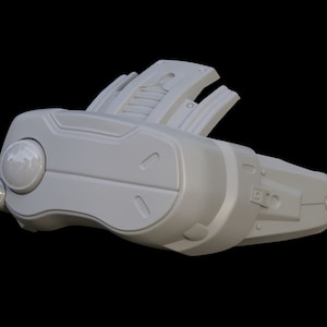 May include: A white, futuristic-looking headset with a large, round lens on the front and a smaller lens on the side. The headset has a textured surface and a series of small, rectangular details.