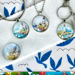 May include: Lighthouse-themed accessories including a bracelet, keychains, and a button. The items feature a colourful lighthouse design on a white background with blue bird and wave patterns. A blue and white patterned pouch is also visible.