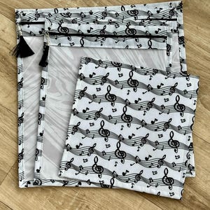 May include: Three reusable zippered bags with a black and white musical note pattern. The bags are made of a clear mesh material and have a black zipper.