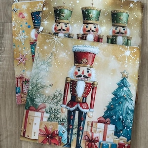 May include: Several Christmas-themed zippered pouches featuring nutcracker soldiers, Christmas trees, and wrapped gifts. The pouches have a gold background with snowflakes and stars. The nutcrackers wear red and green uniforms.
