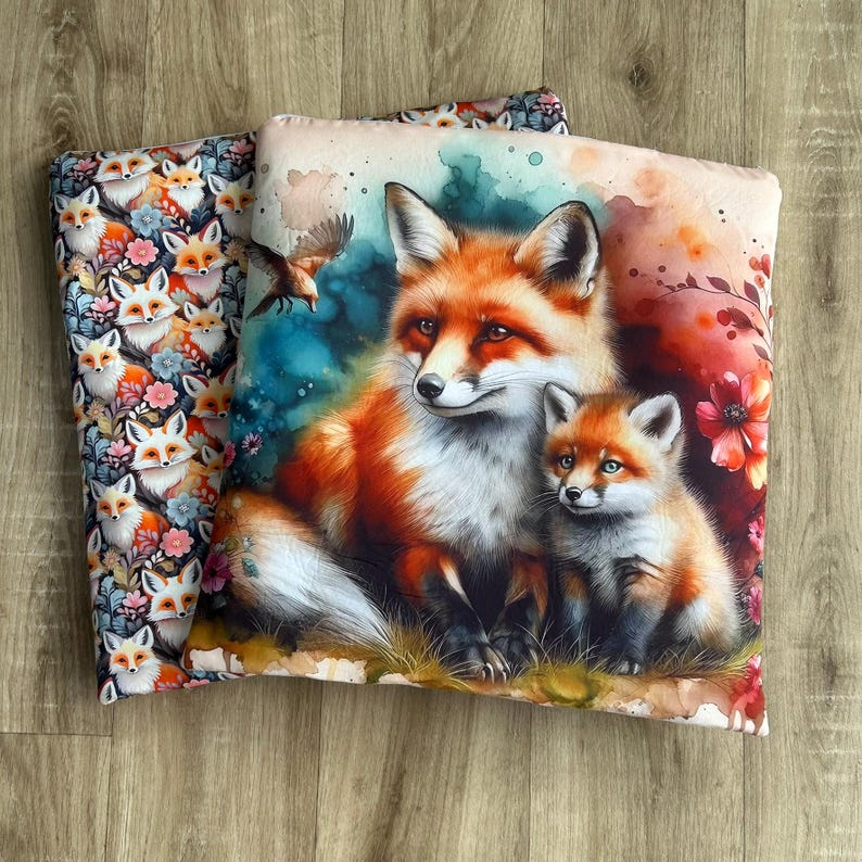 May include: Two decorative throw pillows. One pillow features a repeating pattern of foxes and flowers. The other pillow displays a watercolor painting of a mother fox and her cub, with a bird in flight and floral accents.
