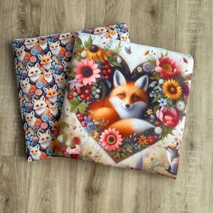 May include: Two decorative pillows. One features a repeating pattern of foxes with flowers in a variety of colors. The other pillow has a fox in the center of a heart-shaped floral arrangement with pink, orange, and yellow flowers.