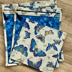 May include: Three zippered pouches with a blue and white butterfly pattern. The pouches are made of fabric and have a zipper closure. The pouches are stacked on top of each other.