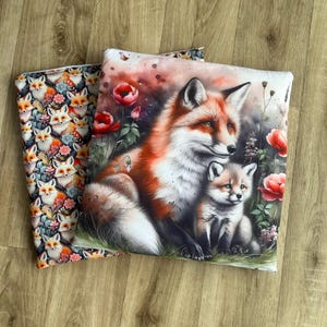 May include: Two decorative throw pillows. One pillow features a repeating pattern of foxes with floral accents. The other pillow displays a watercolor illustration of a mother fox and her cub surrounded by flowers. The foxes have orange and white fur.