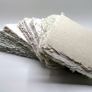 May include: A stack of handmade paper sheets with a rough, textured surface. The paper is a light beige color and has a slightly uneven edge.