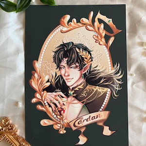 May include: Art print featuring a stylized illustration of a person with dark hair, adorned with a crown and jewelry. The artwork is set against a dark green background, framed by ornate gold embellishments. The name "Cardan" is displayed on a banner.