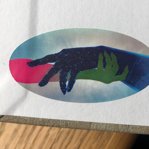 May include: A sticker featuring a blue and green hand reaching out to a black hand with white stars. The hands are set against a blue and pink background.