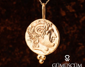 May include: A gold necklace with a round pendant featuring a profile of a person's face. The pendant is attached to a chain with a small ball charm.