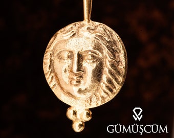 May include: A gold pendant necklace featuring a round coin with a detailed profile of a woman's face. The coin is attached to a chain with a small, decorative bead cluster.