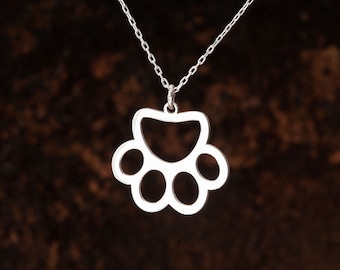 Könnte beinhalten: Eine silberne Halskette mit einem Pfotenabdruck-Anhänger. Der Anhänger ist ein Ausschnitt-Design mit einer glatten, polierten Oberfläche.