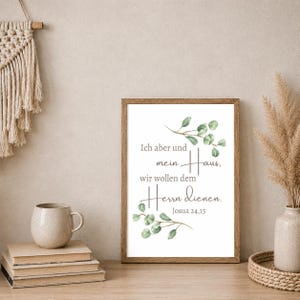 May include: A framed print with the text "Ich aber und mein Haus, wir wollen dem Herrn dienen. Josua 24,15" in a script font. The print is decorated with green eucalyptus branches and is displayed on a wooden surface.