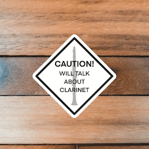 May include: A white diamond-shaped sticker with a black border and a black silhouette of a clarinet. The sticker reads "CAUTION! WILL TALK ABOUT CLARINET".