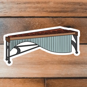 May include: A sticker of a wooden marimba with a blue and white resonating chamber. The marimba is on a black stand with wheels.
