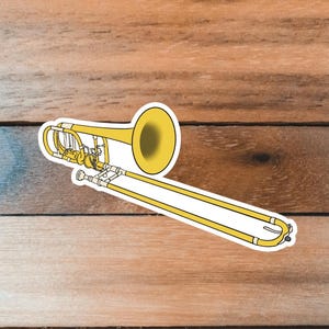 May include: A yellow trombone sticker with black outlines. The trombone is a brass instrument with a slide and bell. The sticker is on a wooden surface.
