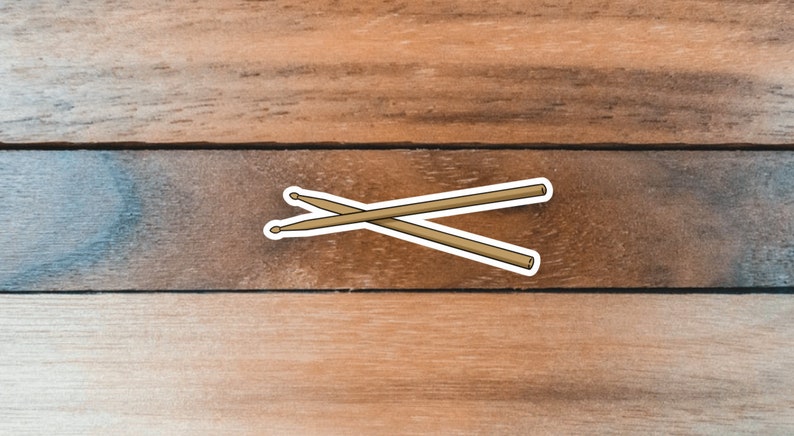 Puede incluir: Dos baquetas de bater&iacute;a de madera marr&oacute;n cruzadas sobre un fondo de madera.