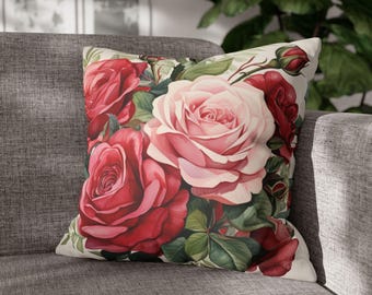 May include: Square throw pillow featuring a watercolor floral design. The pillow showcases a bouquet of red and pink roses with green leaves against a cream background. The pillow is placed on a gray sofa.