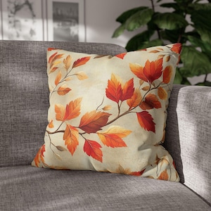 May include: A decorative throw pillow with a beige background and a pattern of orange and red leaves. The leaves are arranged in a branch-like pattern.