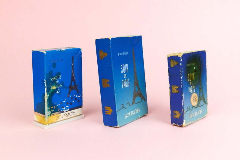 Puede incluir: Tres cajas de perfume vintage azules y doradas con el texto "Soir de Paris" y el logotipo de Bourjois. Las cajas presentan un gr&aacute;fico de la Torre Eiffel.