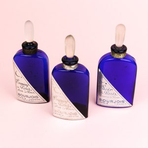 May include: Three blue glass bottles with silver caps and labels. The labels read "Evening in Paris" and "Soir de Paris" with the Bourjois logo.