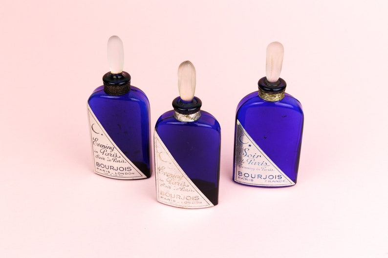 May include: Three blue glass bottles with silver caps and labels. The labels read "Evening in Paris" and "Soir de Paris" with the Bourjois logo.