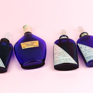 May include: Four blue glass bottles of perfume with silver labels. The bottles are labeled "Evening in Paris" and "Soir de Paris" with the brand name Bourjois.
