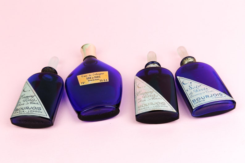 May include: Four blue glass bottles of perfume with silver labels. The bottles are labeled "Evening in Paris" and "Soir de Paris" with the brand name Bourjois.