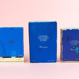 Puede incluir: Tres cajas azules con bordes dorados. Las cajas est&aacute;n etiquetadas con el texto "L'Excellence de nos produits nous a conquis les march&eacute;s du monde" y "Bourjois".