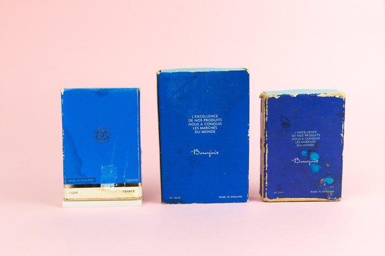 Puede incluir: Tres cajas azules con bordes dorados. Las cajas est&aacute;n etiquetadas con el texto "L'Excellence de nos produits nous a conquis les march&eacute;s du monde" y "Bourjois".