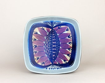 May include: A square ceramic serving dish with a blue and brown geometric design. The design features a central motif of overlapping circles and lines, surrounded by stylized leaves and flowers.