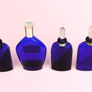 May include: Four cobalt blue glass perfume bottles with silver and gold accents. The bottles have different shapes and sizes.