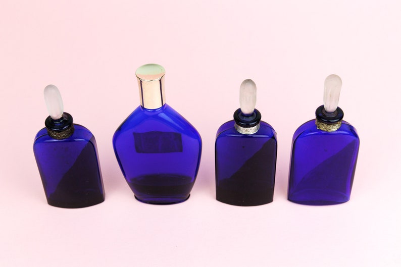 May include: Four cobalt blue glass perfume bottles with silver and gold accents. The bottles have different shapes and sizes.