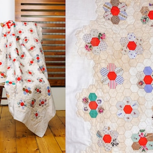May include: A white quilt with a patchwork design featuring red, blue, and green floral motifs. The quilt is folded and draped over a wooden chair.