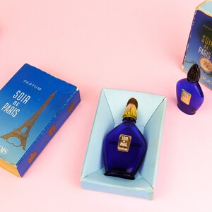 Puede incluir: Tres cajas azules con letras doradas y un dise&ntilde;o de la Torre Eiffel dorada. Las cajas contienen botellas de perfume en miniatura etiquetadas como "Soir de Paris" de Bourjois.