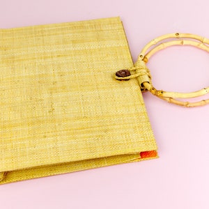 Puede incluir: Un bolso de mano tejido de color marr&oacute;n claro con un asa de bamb&uacute; de doble anillo.