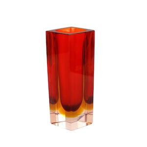 May include: A tall, rectangular red glass vase with a square opening. The vase has a clear, transparent base and a gradient of colors, transitioning from red to orange and yellow. The vase is approximately 10 inches tall.