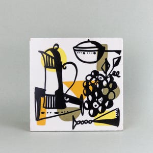 May include: Square ceramic tile with a mid-century modern design. The artwork features black, yellow, and white illustrations of a coffee pot, grapes, and a cooking pot. The tile has a clean, minimalist aesthetic, suitable for kitchen or dining decor.