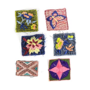 May include: A collection of six embroidered patches with floral and geometric designs. The patches feature various colors, including blue, pink, yellow, and green, on a white background. The embroidery appears to be hand-stitched.