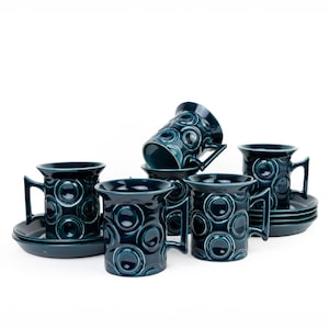 May include: Set of six teal blue ceramic coffee mugs with a circular pattern. Each mug has a matching saucer.