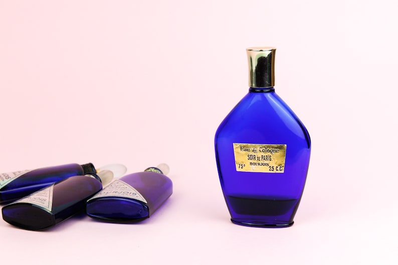 May include: Four blue glass bottles of cologne, one with a gold cap and a label that reads "Eau de Cologne Soir de Paris Bourjois 75* 25 c.c."