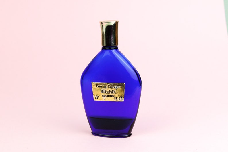 May include: A blue glass bottle of cologne with a gold cap and a gold label that reads "Eau de Cologne SOIR de PARIS BOURJOIS 25 C.C. 75&deg;".