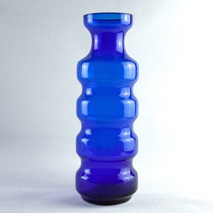 May include: A tall, cobalt blue glass vase with a textured, rippled design. The vase has a wide mouth and a narrow base.