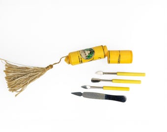 May include: A yellow metal case with a tassel and a label that reads "The Original" contains four small tools with yellow handles. The tools are a nail file, a cuticle pusher, and two small spatulas.