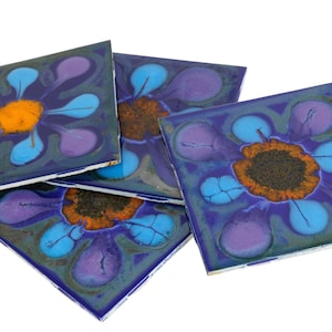 May include: Four square ceramic tiles with a floral design. Each tile features a central orange flower surrounded by blue and purple petal shapes on a dark blue background. The tiles are approximately 6 inches square.